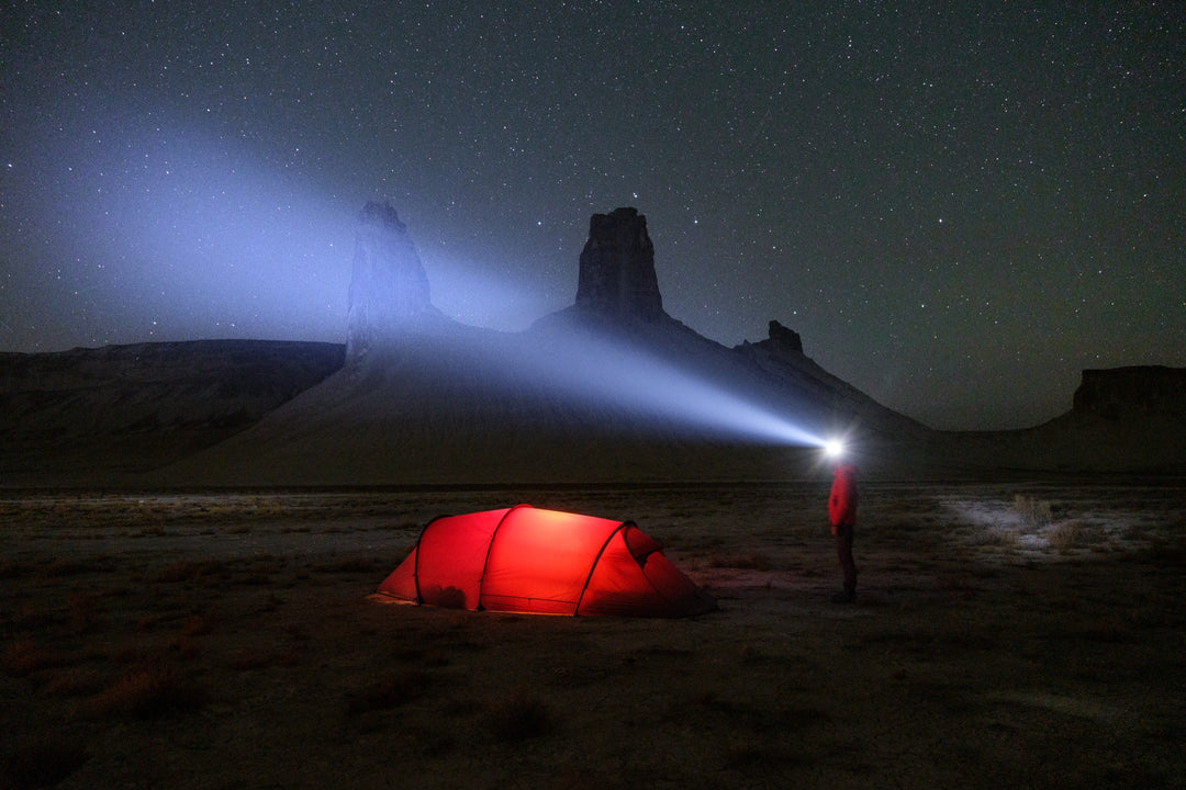 Camper using a Zweibrüder head torch to light rock spires beside a tent under a starlit sky