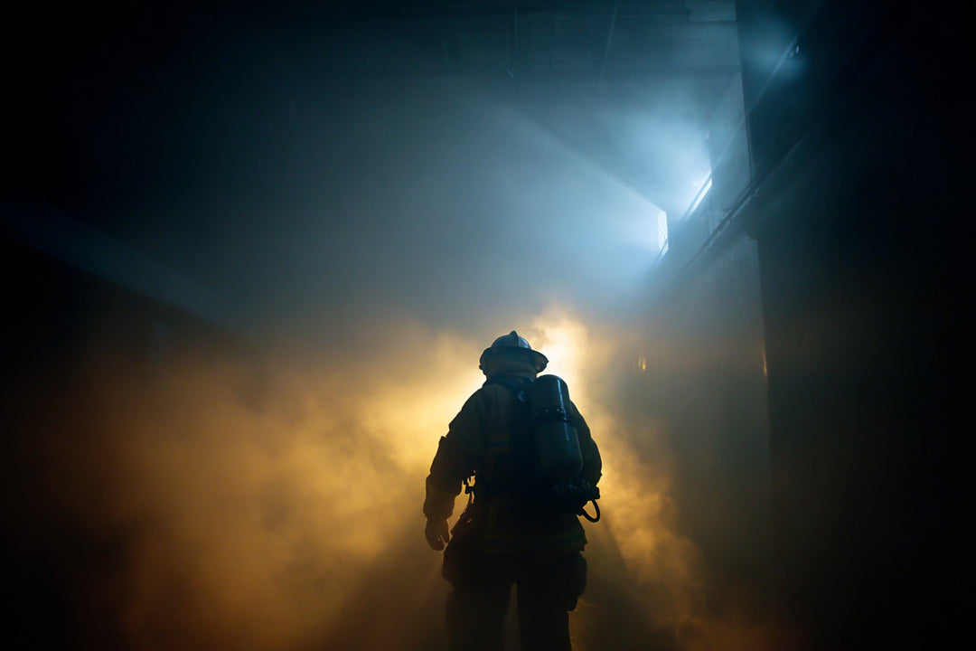Firefighter silhouetted in smoke, helmet torch beam cutting through the haze